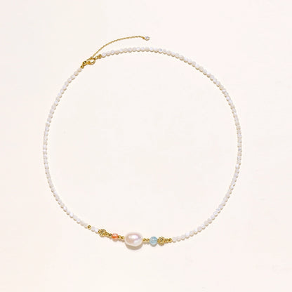 Delicate white beaded necklace with baroque pearl center, gold accents, and coral and aqua gemstones on cream background.