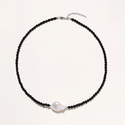 Beaded black agate necklace with iridescent baroque freshwater pearl centerpiece on cream background.